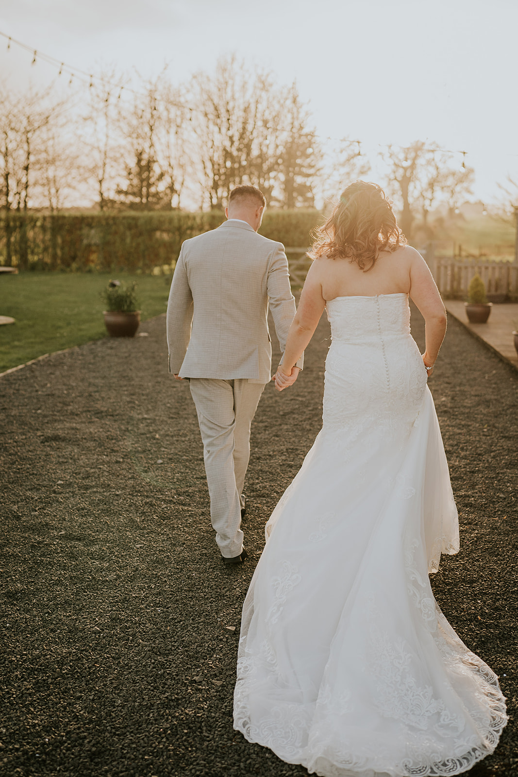 Bride and groom walking hand in hand along a rustic countryside path at sunset at Vallum Weddings, with lush greenery, romantic ambiance, and a scenic outdoor wedding venue in Northumberland.