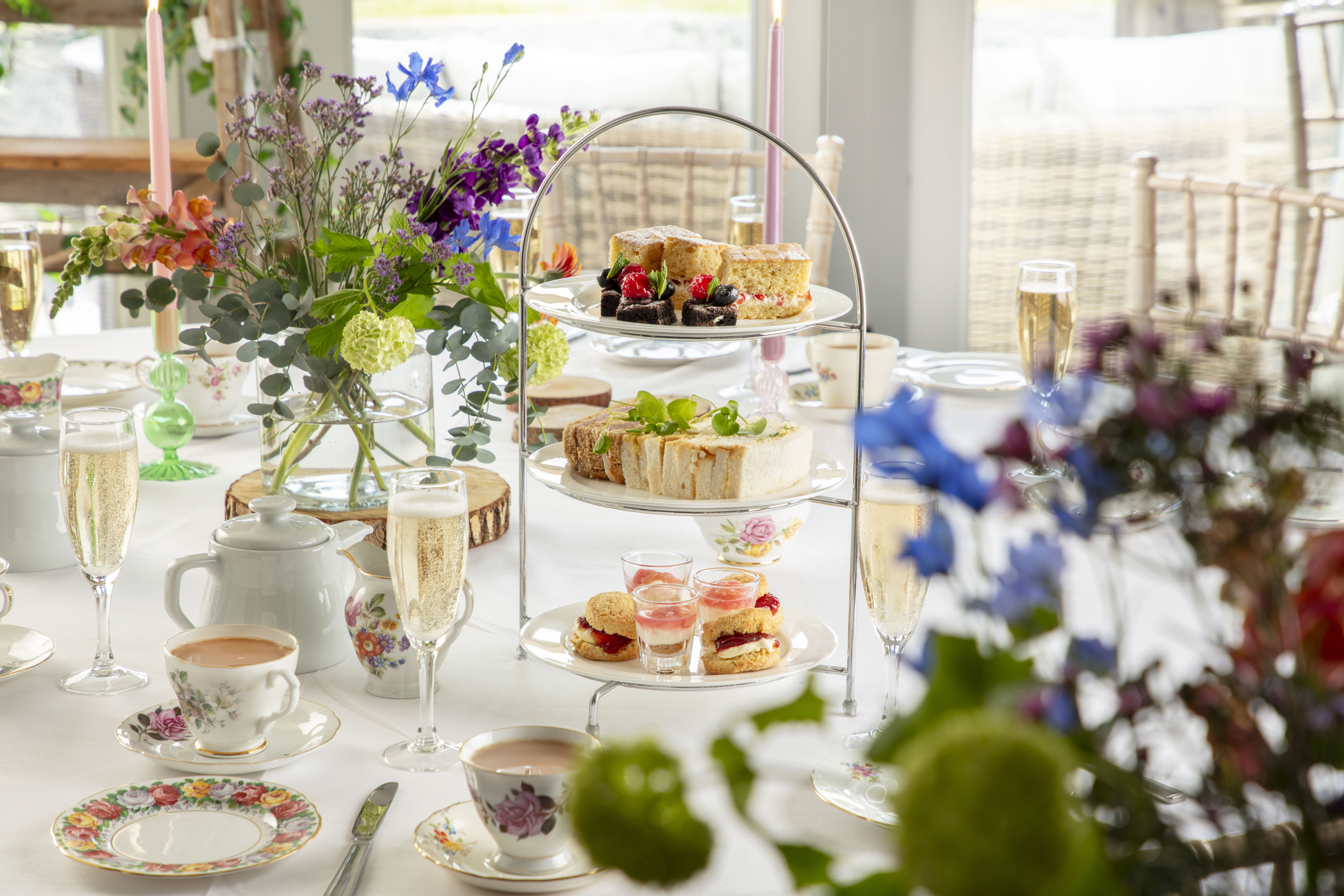 Elegant afternoon tea setup at Vallum Weddings with floral china, champagne flutes, and a tiered cake stand of scones and desserts, set against a romantic countryside backdrop in Northumberland.