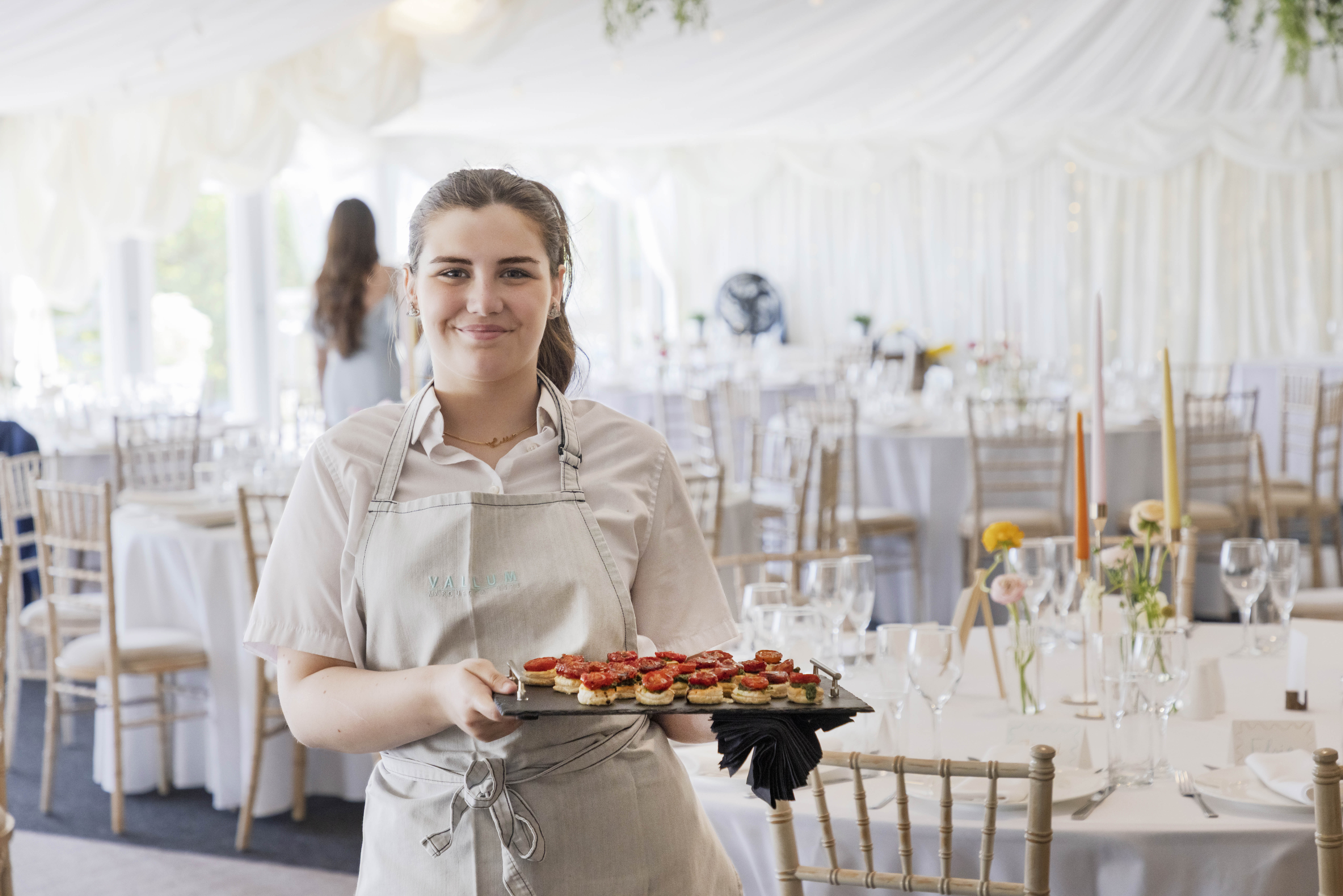 Hospitality moment at Vallum Weddings: waiter with appetizer tray amid an ambient reception setup with crisp tablecloths and rustic-luxe décor in Northumberland.