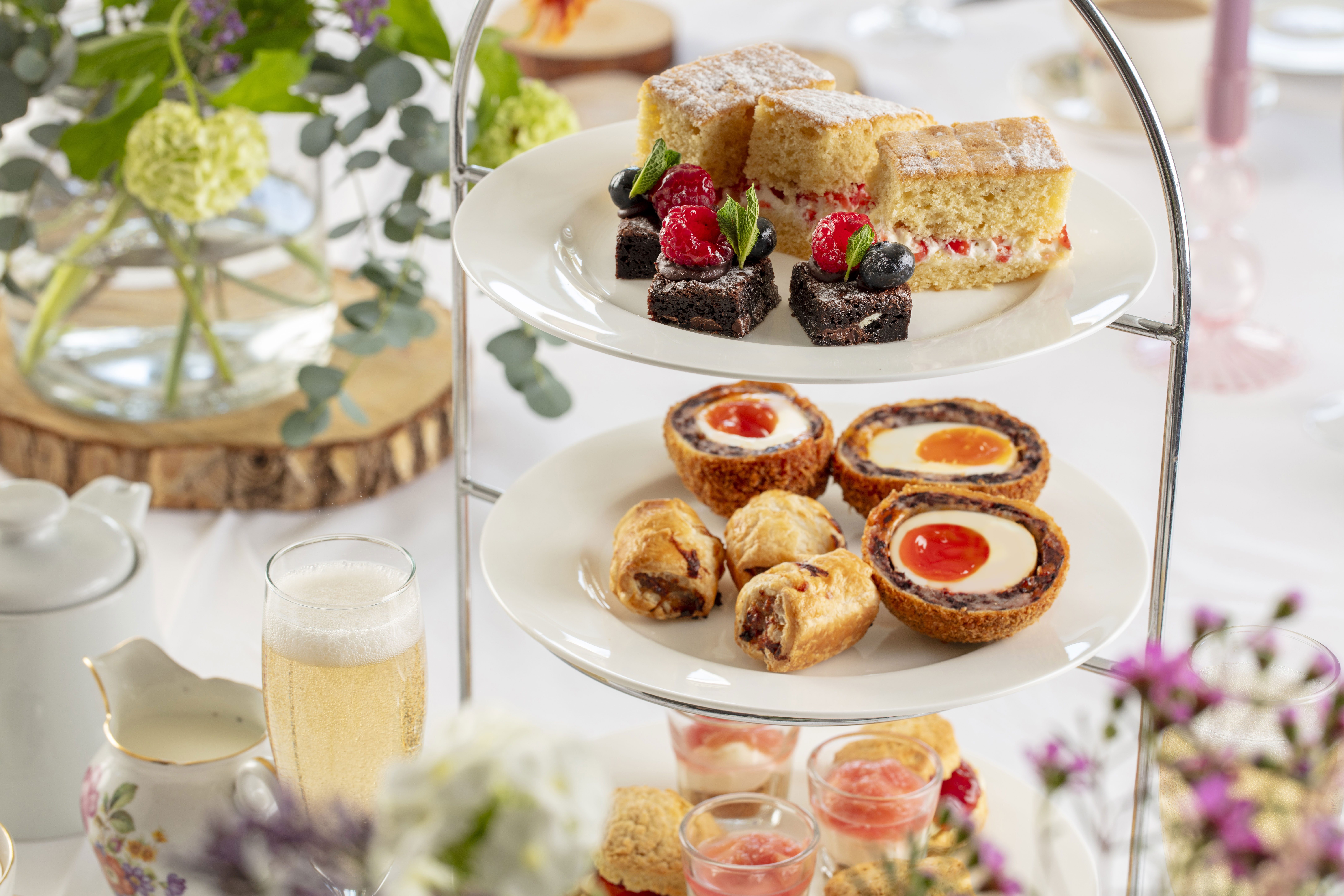 Three-tiered afternoon tea stand at Vallum Weddings, featuring scones, sausage rolls, sponge cakes, and chocolate brownies, paired with champagne and tea