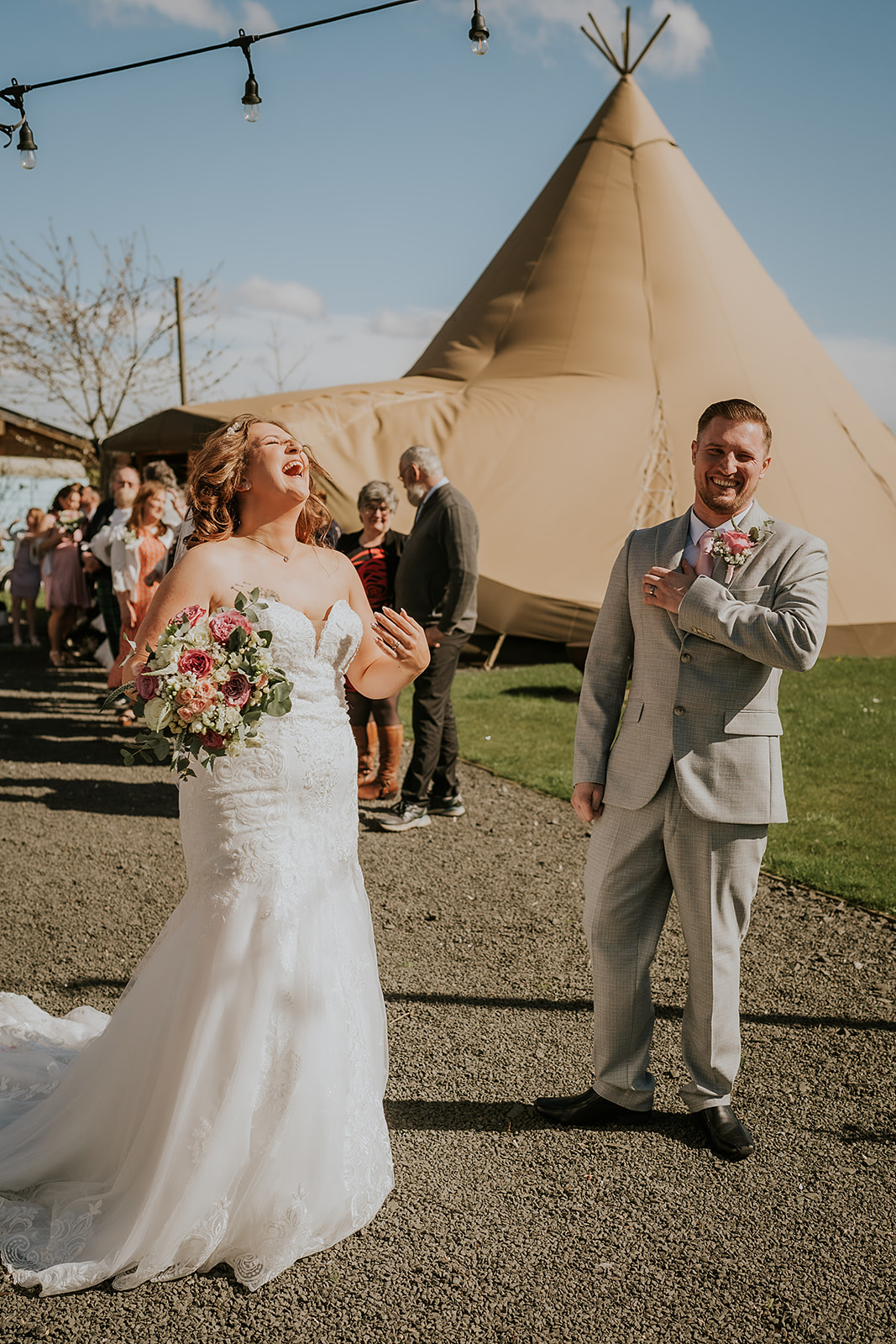 Bride and groom sharing a moment on a gravel path at Vallum Weddings, surrounded by guests and glowing string lights, under clear evening skies with warm golden hour light and a gentle summer breeze.